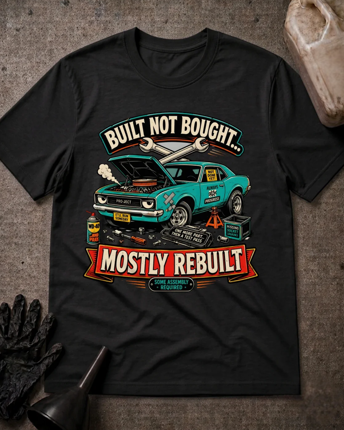 Front of black T-shirt with a teal project car, open hood and tools graphic reading “Built Not Bought… Mostly Rebuilt.”