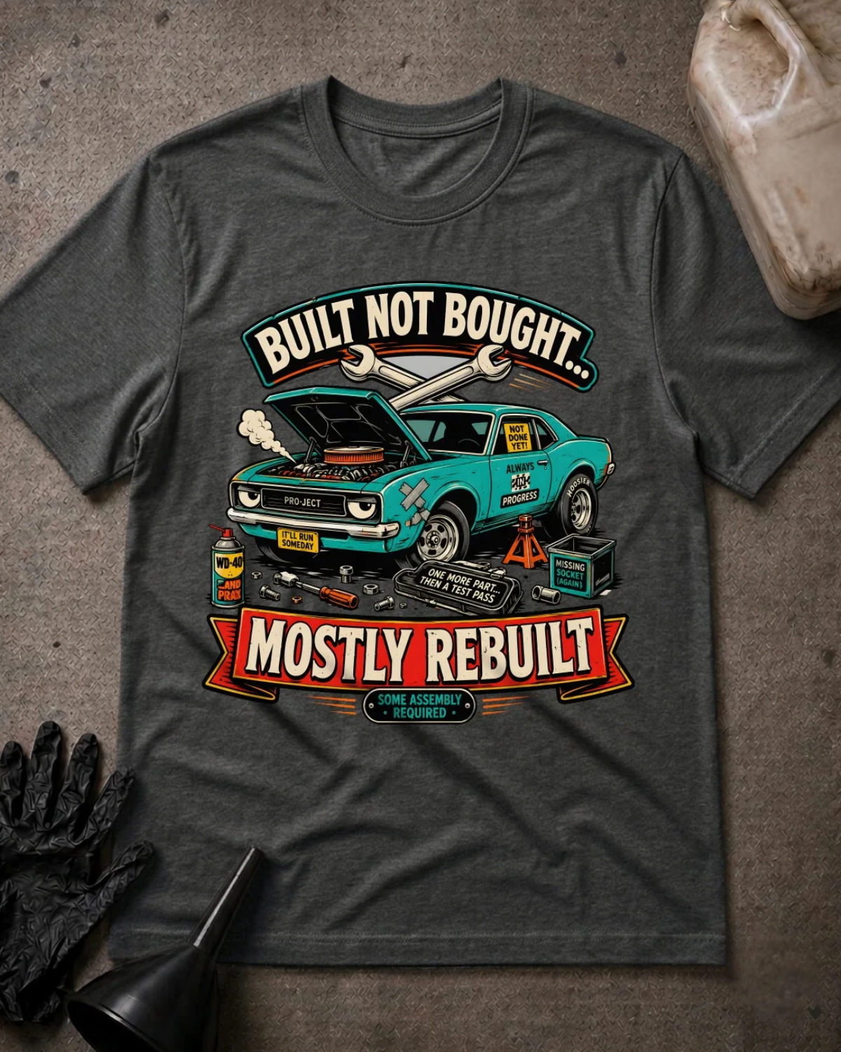 Front of dark grey heather T-shirt with a teal project car, open hood and tools graphic reading “Built Not Bought… Mostly Rebuilt.”