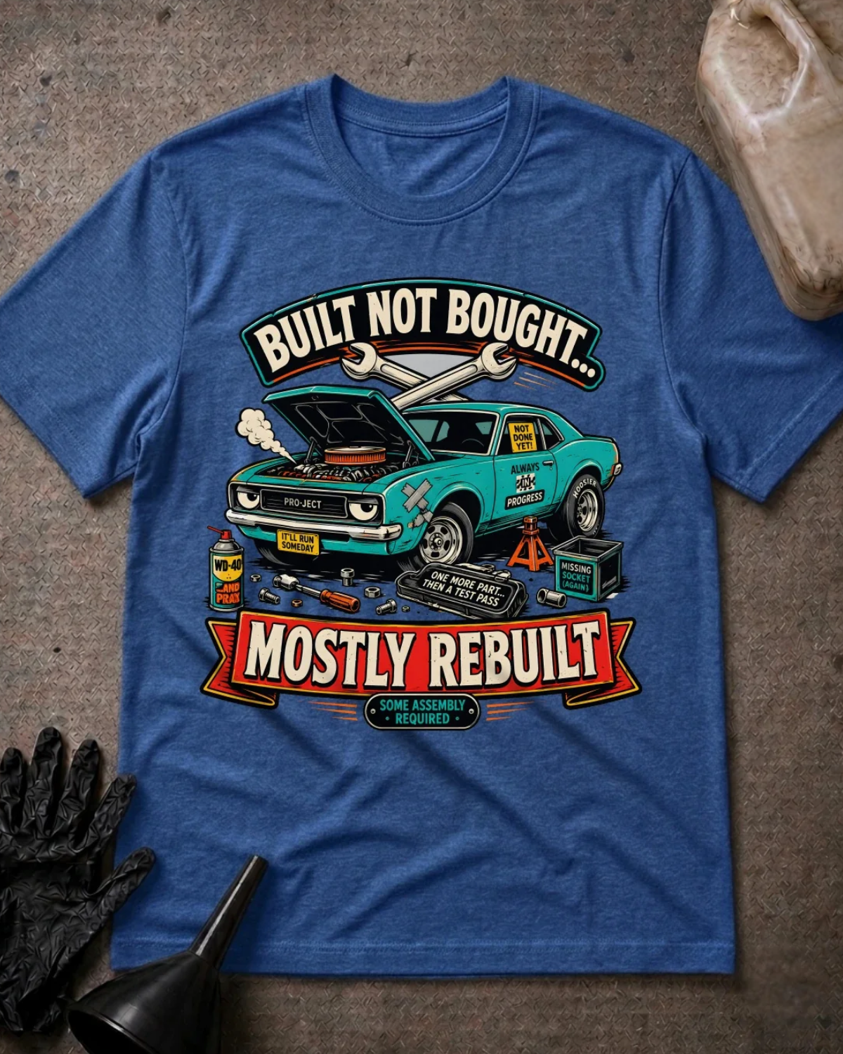 Front of heather true royal blue T-shirt with a teal project car, open hood and tools graphic reading “Built Not Bought… Mostly Rebuilt.”