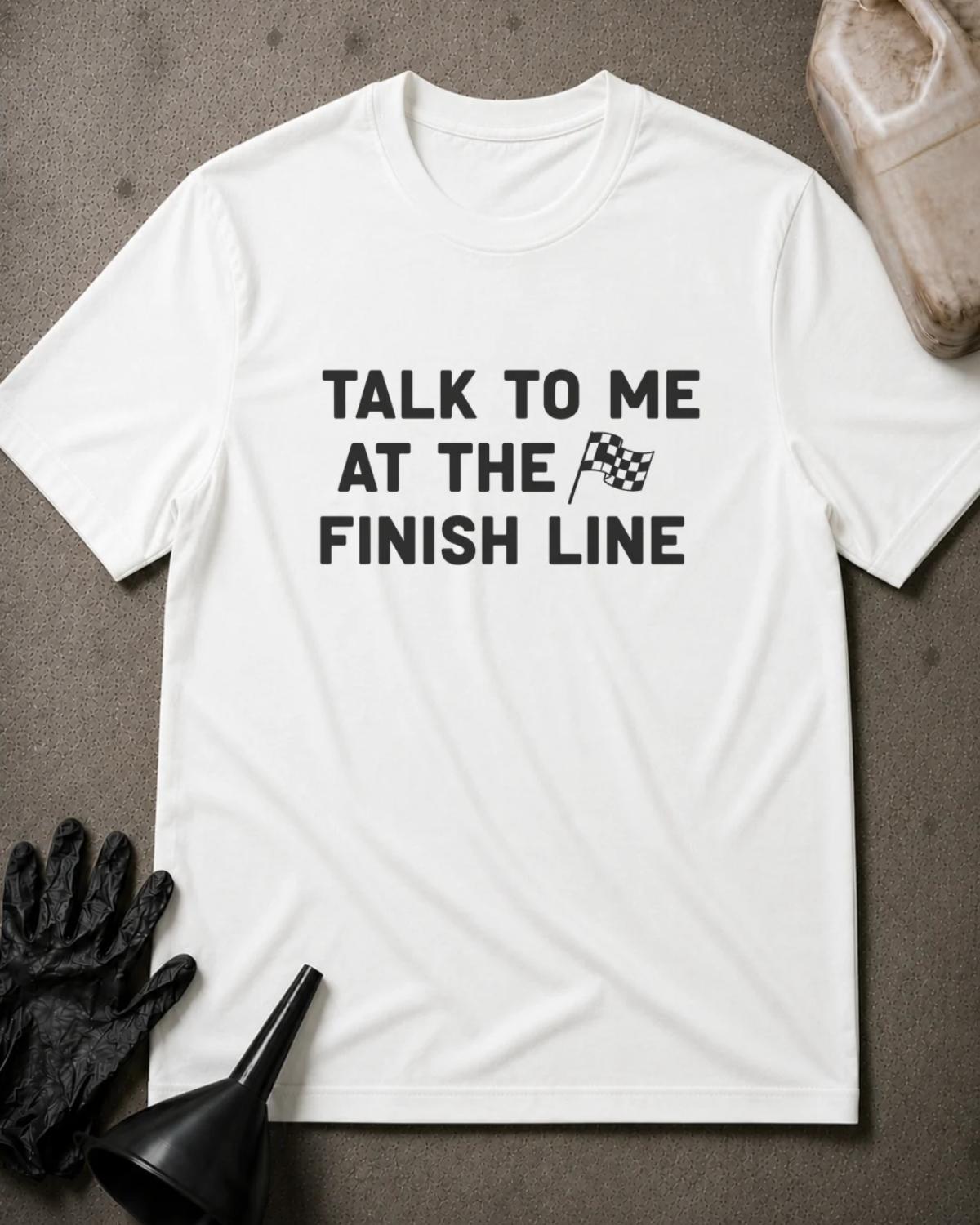 White racing T-shirt featuring bold black lettering reading “Talk to me at the finish line” with a small checkered flag graphic.