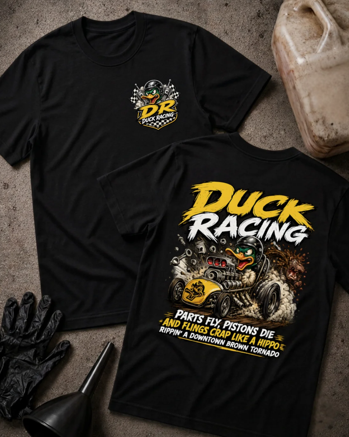 Front and back of black Duck Racing T-shirt with a checkered-flag chest emblem and helmeted cartoon duck driving a yellow hot rod amid smoke and flying engine parts.