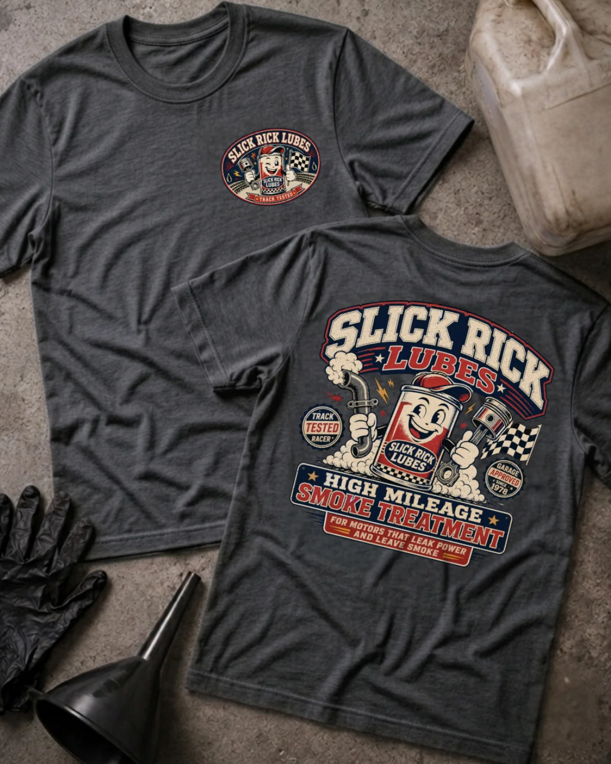 Front and back of dark grey heather Slick Rick Lubes T-shirt with a chest logo and cartoon motor oil can holding a piston and exhaust pipe above “High Mileage Smoke Treatment.”
