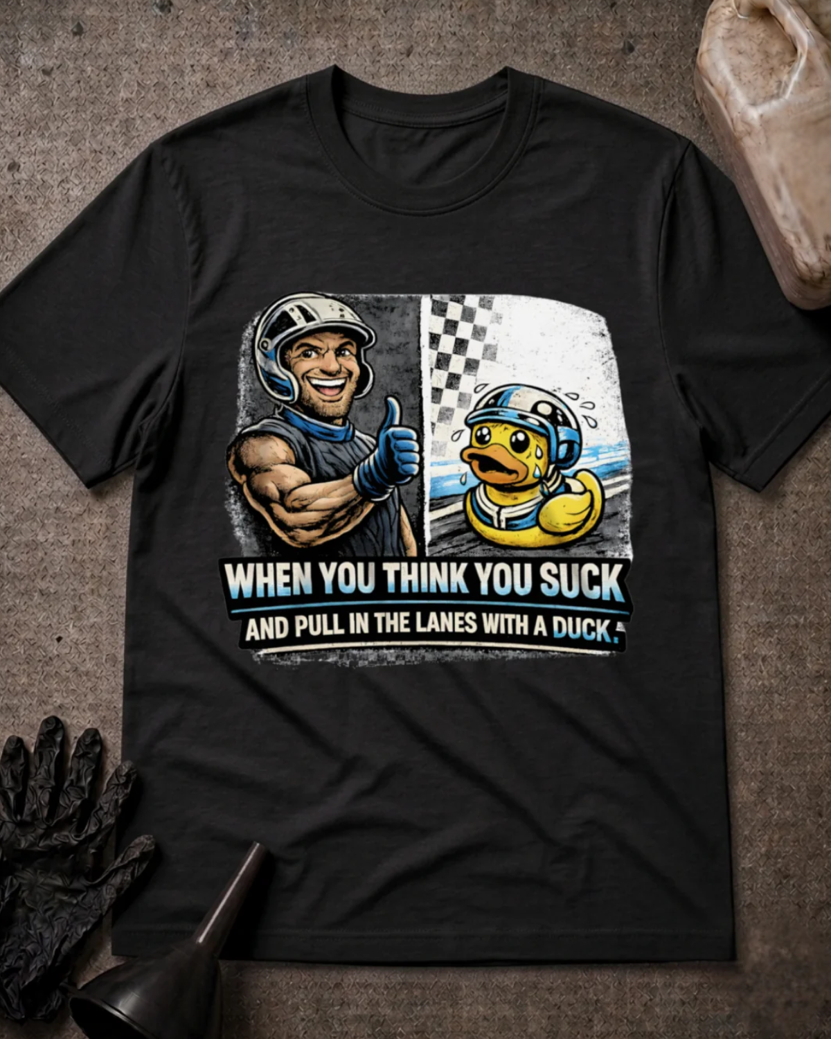 Front of black T-shirt with a smiling racer giving a thumbs-up beside a nervous helmeted duck, reading “When You Think You Suck and Pull in the Lanes with a Duck.”