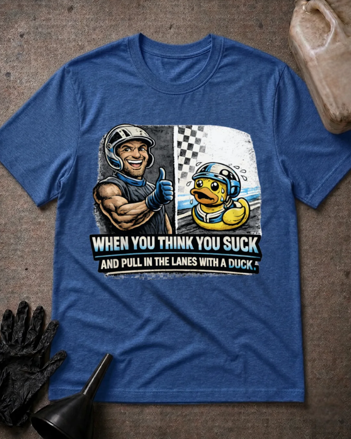 Front of heather true royal blue T-shirt with a smiling racer giving a thumbs-up beside a nervous helmeted duck, reading “When You Think You Suck and Pull in the Lanes with a Duck.”