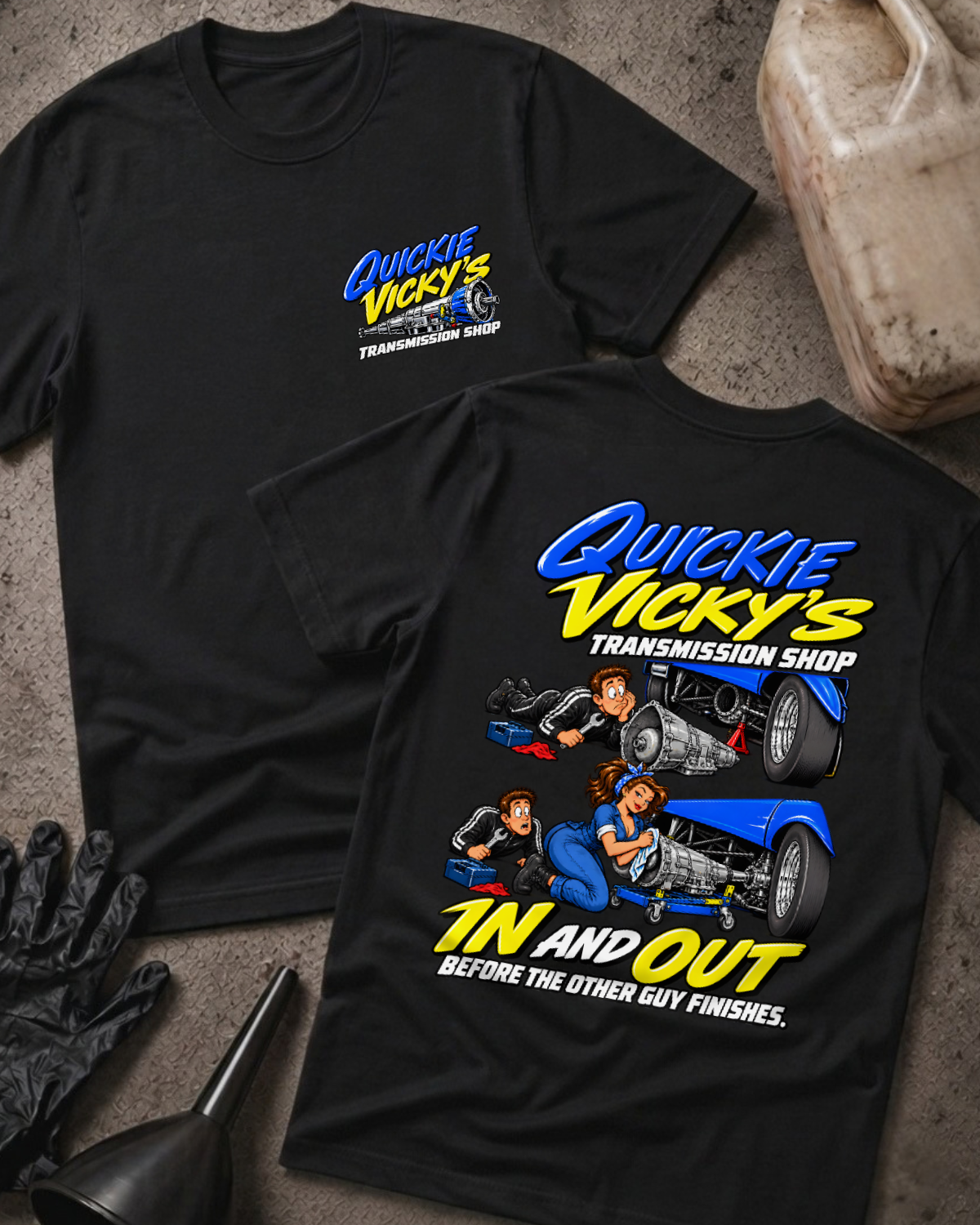 Black Quickie Vicky’s Transmission Shop T-shirt showing the front chest logo and back cartoon of a woman mechanic rebuilding a transmission under a blue hot rod, “In and Out Before the Other Guy Finishes,” with gloves, funnel, and oil jug props.