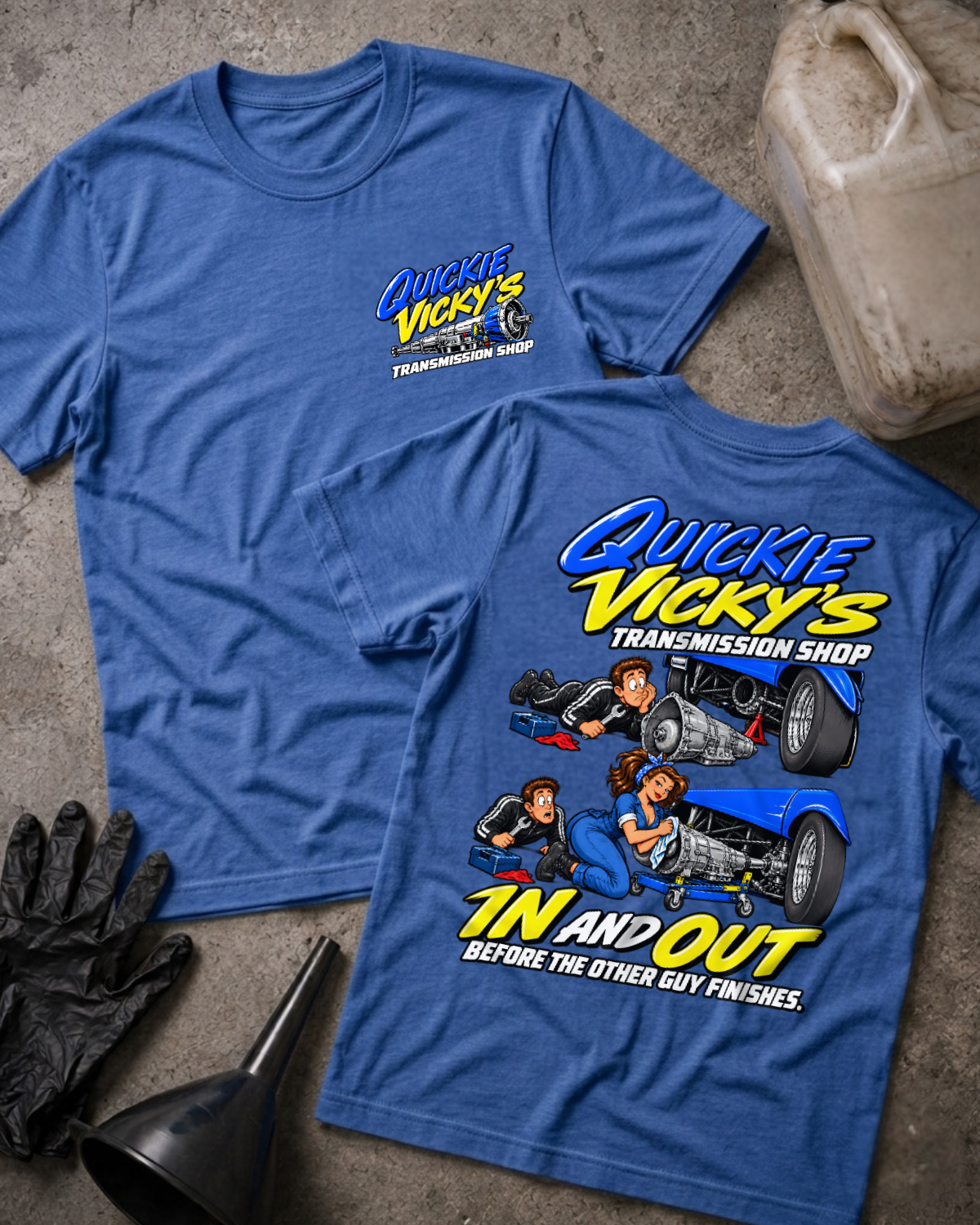 Heather royal blue Quickie Vicky’s Transmission Shop T-shirt showing the front chest logo and back cartoon of a woman mechanic rebuilding a transmission under a blue hot rod, “In and Out Before the Other Guy Finishes,” with gloves, funnel, and oil jug.
