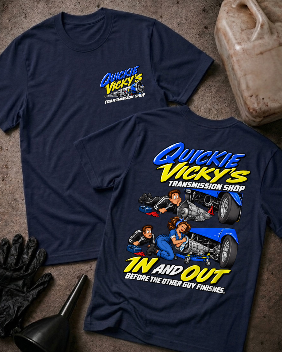 Navy Quickie Vicky’s Transmission Shop T-shirt showing the front chest logo and back cartoon of a woman mechanic rebuilding a transmission under a blue hot rod, “In and Out Before the Other Guy Finishes,” with gloves, funnel, and oil jug props.