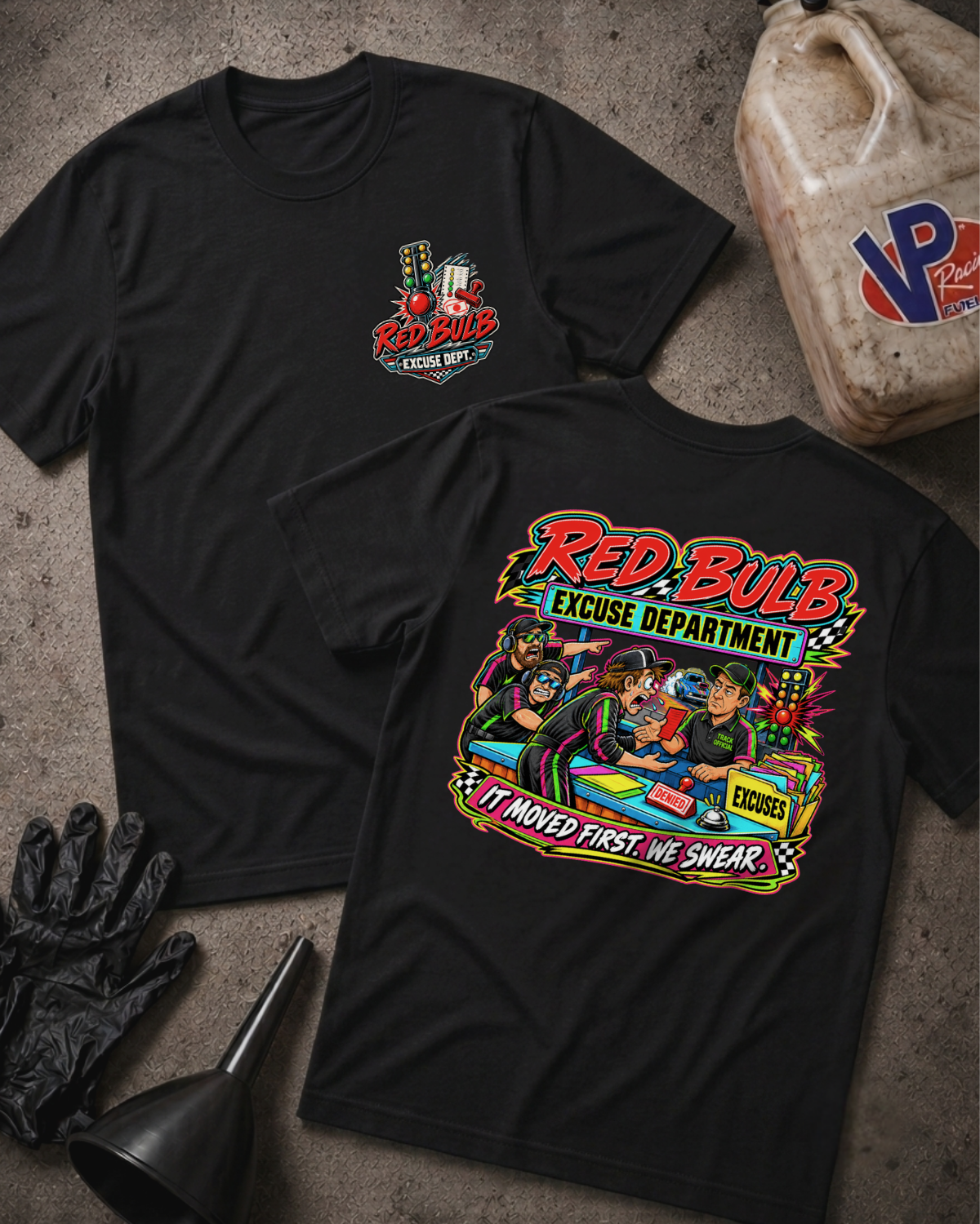 Two black graphic T-shirts laid flat on a textured gray surface, with automotive-themed printed artwork and the text 'RED BULB EXCUSE DEPARTMENT.' One shirt shows a small circular chest logo, and the other shows a large back graphic with an illustration and the phrase 'IT MOVED FIRST. WE SWEAR.'