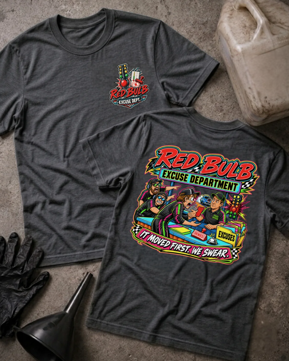 Front and back of Red Bulb Excuse Department dark grey heather drag racing T-shirt with chest logo, racers arguing at an excuse desk beside a red starting light, and “It moved first. We swear.” slogan.