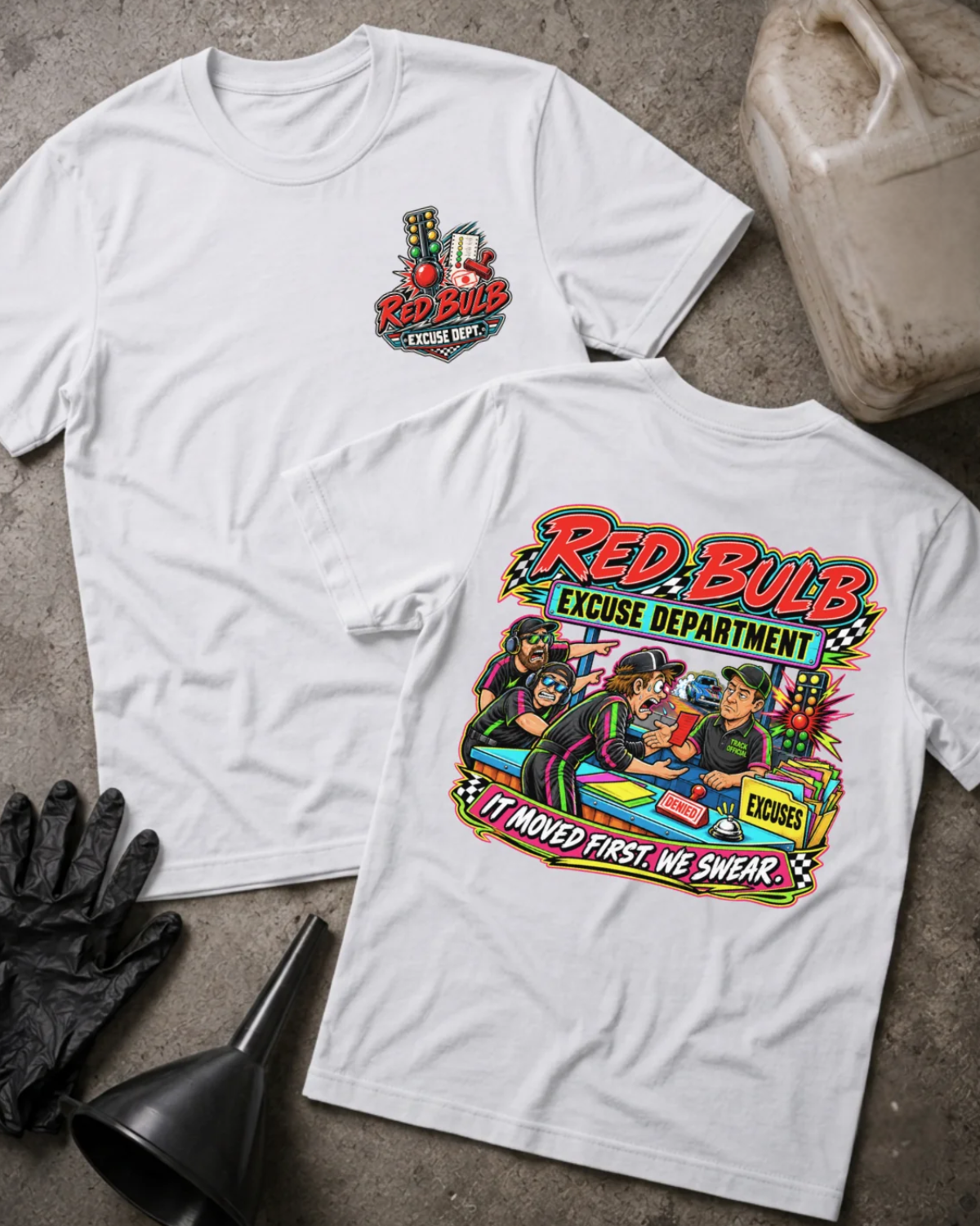 Front and back of Red Bulb Excuse Department white drag racing T-shirt with chest logo, racers arguing at an excuse desk beside a red starting light, and “It moved first. We swear.” slogan.