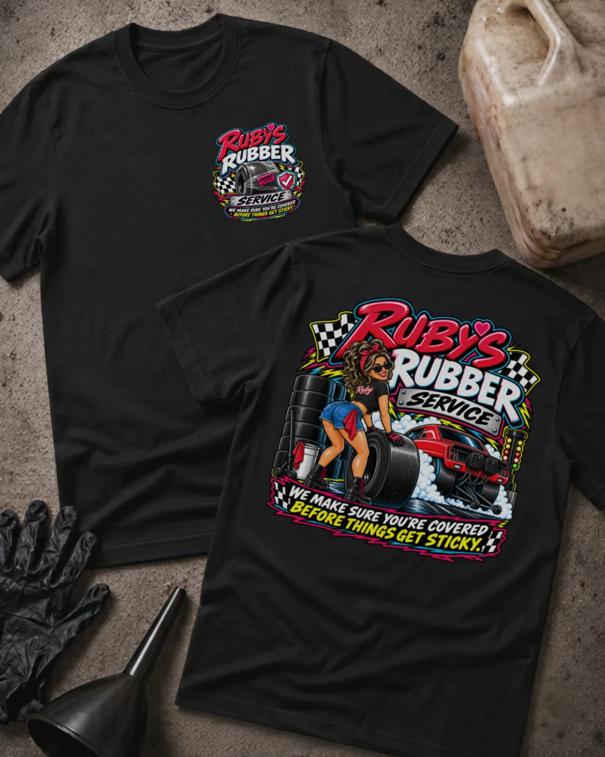 Front and back of Ruby’s Rubber Service black T-shirt with chest logo, woman beside racing tires and a red drag car, and “We make sure you’re covered before things get sticky” slogan.