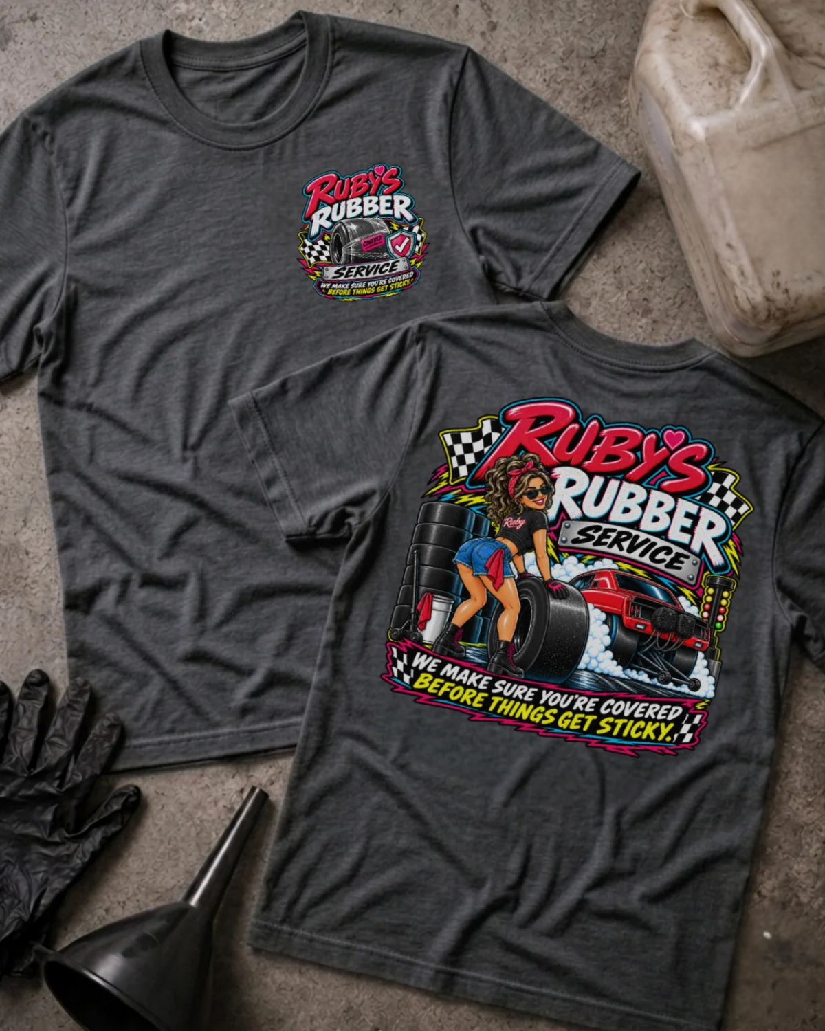 Front and back of Ruby’s Rubber Service dark grey heather T-shirt with chest logo, woman beside racing tires and a red drag car, and “We make sure you’re covered before things get sticky” slogan.