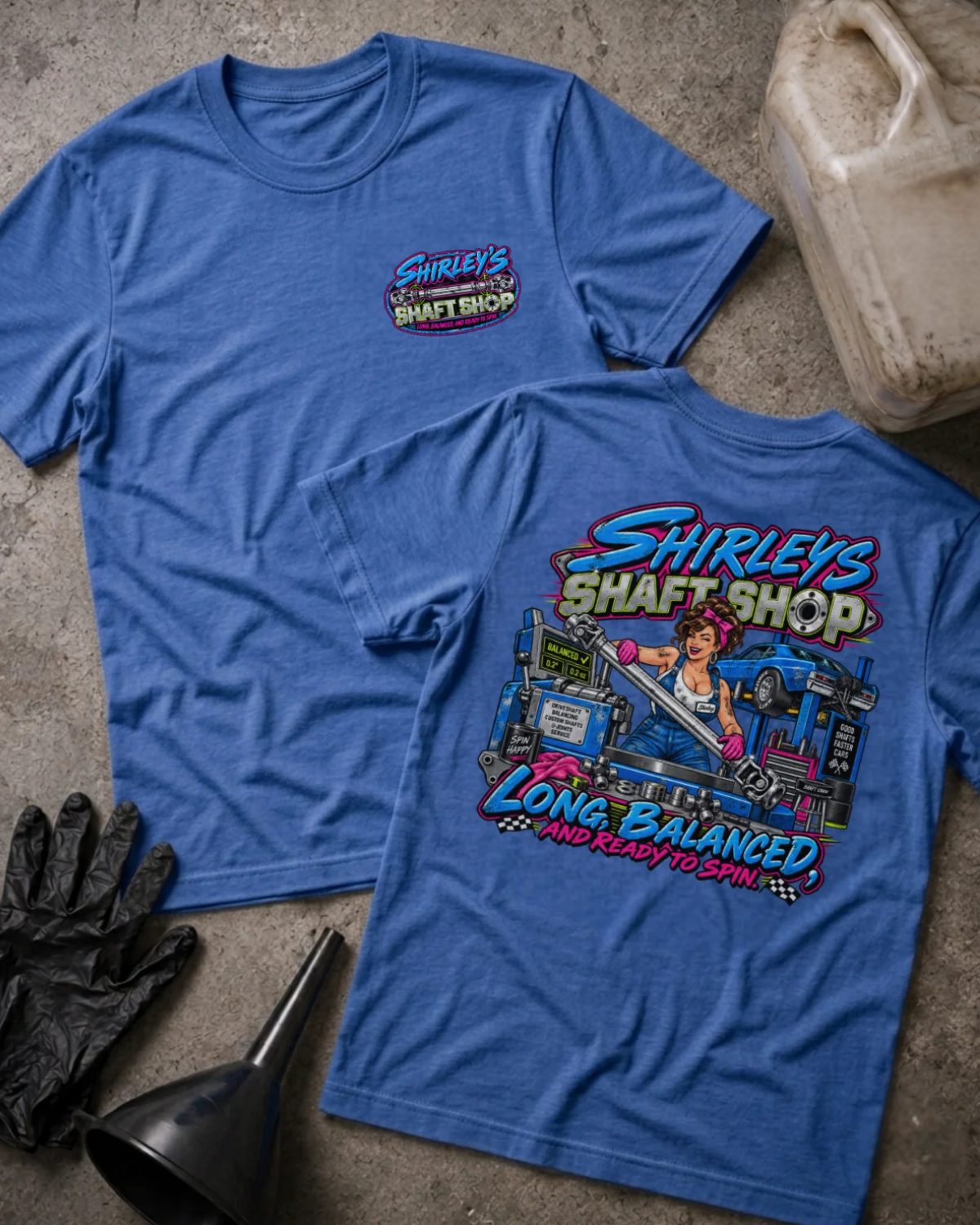 Front and back of Shirley’s Shaft Shop heather true royal T-shirt with chest logo, woman holding a driveshaft in a workshop, and “Long, balanced, and ready to spin” slogan.