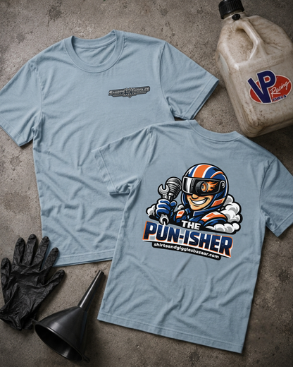 Two light blue graphic T-shirts laid flat on a textured gray surface, with a large cartoon racecar driver graphic on the back and a smaller chest logo on the front. Black gloves, a black funnel, and a VP Racing jug are placed around them as styling props.