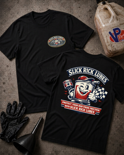Two black graphic T-shirts laid flat on a textured gray surface, showing the front and back designs for 'Slick Rick Lubes'. The front has a small circular chest logo, and the back features a large cartoon grease can graphic with a smiling face and text.