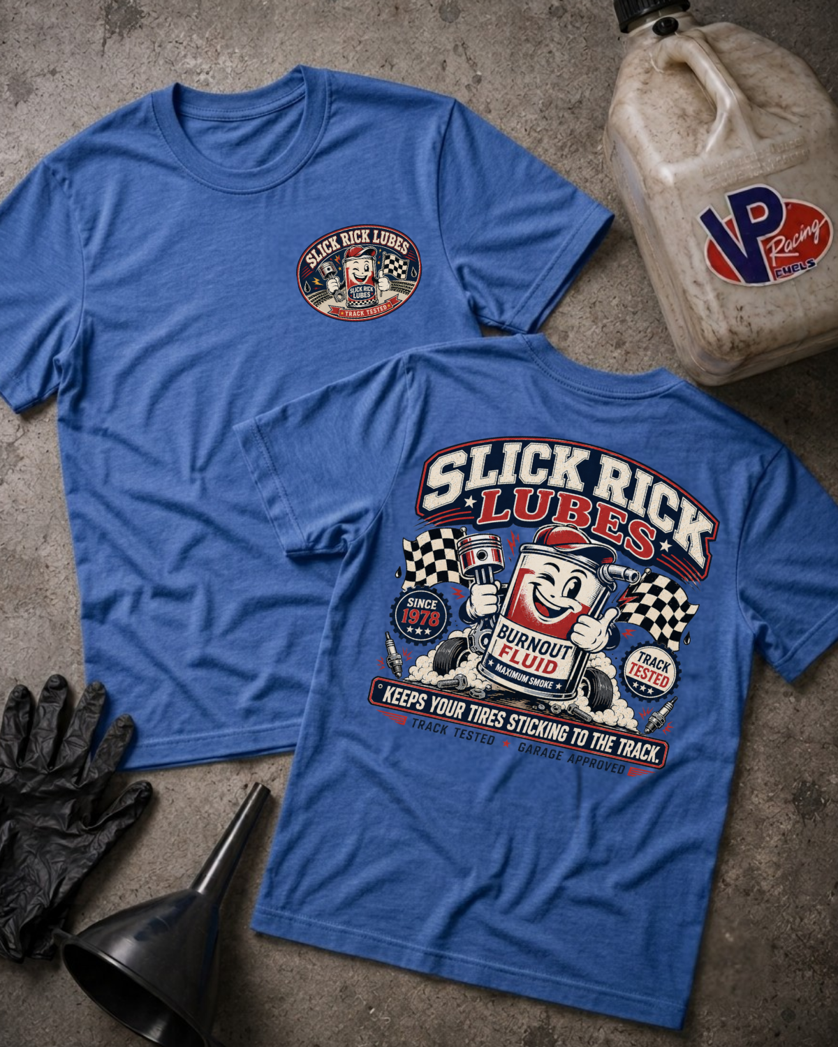 Two blue short-sleeve T-shirts laid flat on a textured gray surface, showing the front and back of a Slick Rick Lubes graphic design. A black oil change glove, funnel, and a plastic jugs with VP Racing logos are arranged around them as styling props.