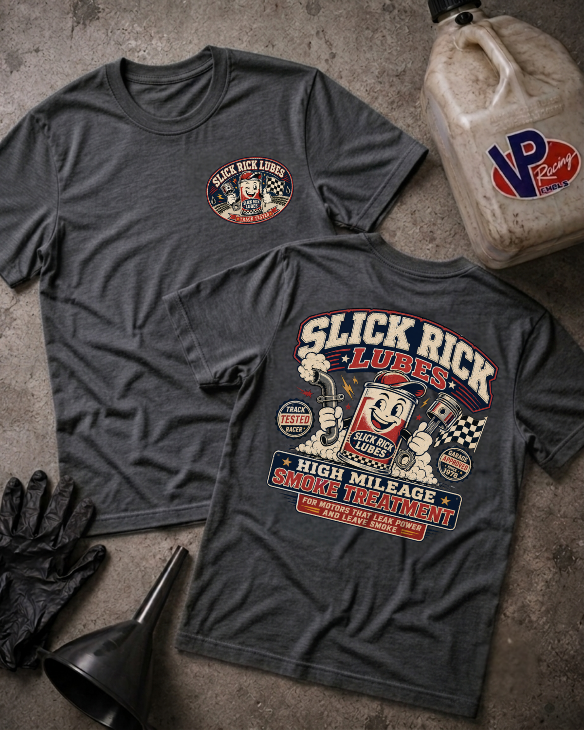 Two dark heather gray graphic T-shirts laid flat on a concrete floor, showing the front and back designs for 'Slick Rick Lubes'. A vintage VP Racing fuel jug, black gloves, and a black funnel are styled around the shirts.