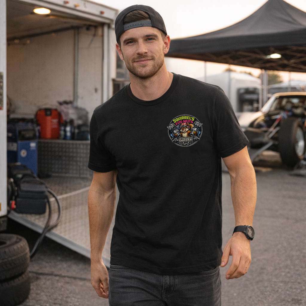 Man wearing a black t-shirt with a 'Squirrel's Lug Nuts' logo, standing in a drag race pit crew area with vehicles and equipment.