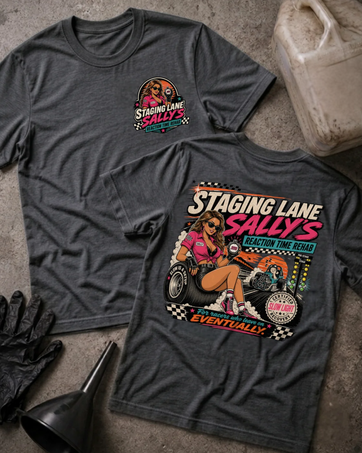 Front and back of Staging Lane Sally’s dark grey heather T-shirt with chest logo, woman holding a stopwatch seated on a racing tire, and “For racers who leave on eventually” slogan.