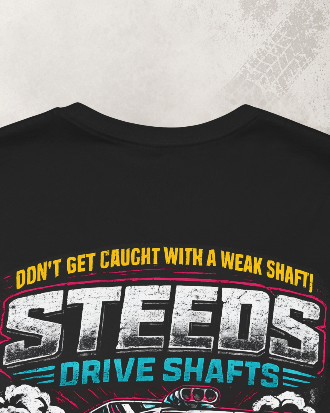 Black t-shirt with close up detail of colorful text and graphic design on a textured gray background