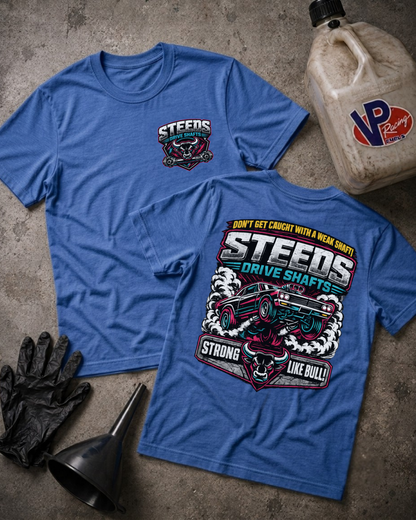 Two blue graphic T-shirts laid flat on a concrete surface, one showing the front chest logo and the other the large back graphic. Black gloves and a black funnel sit beside them, with a plastic jug in the upper right.