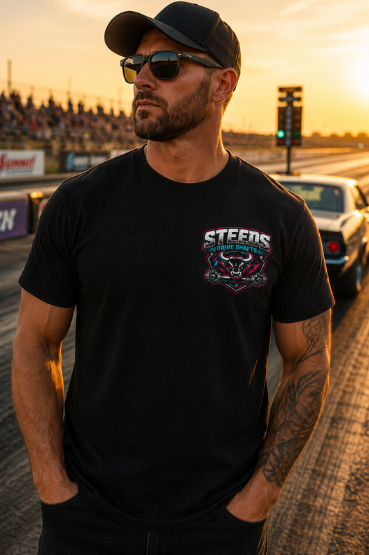 Man wearing a black t-shirt with a 'Steeds Drive Shafts' logo on a race track at sunset