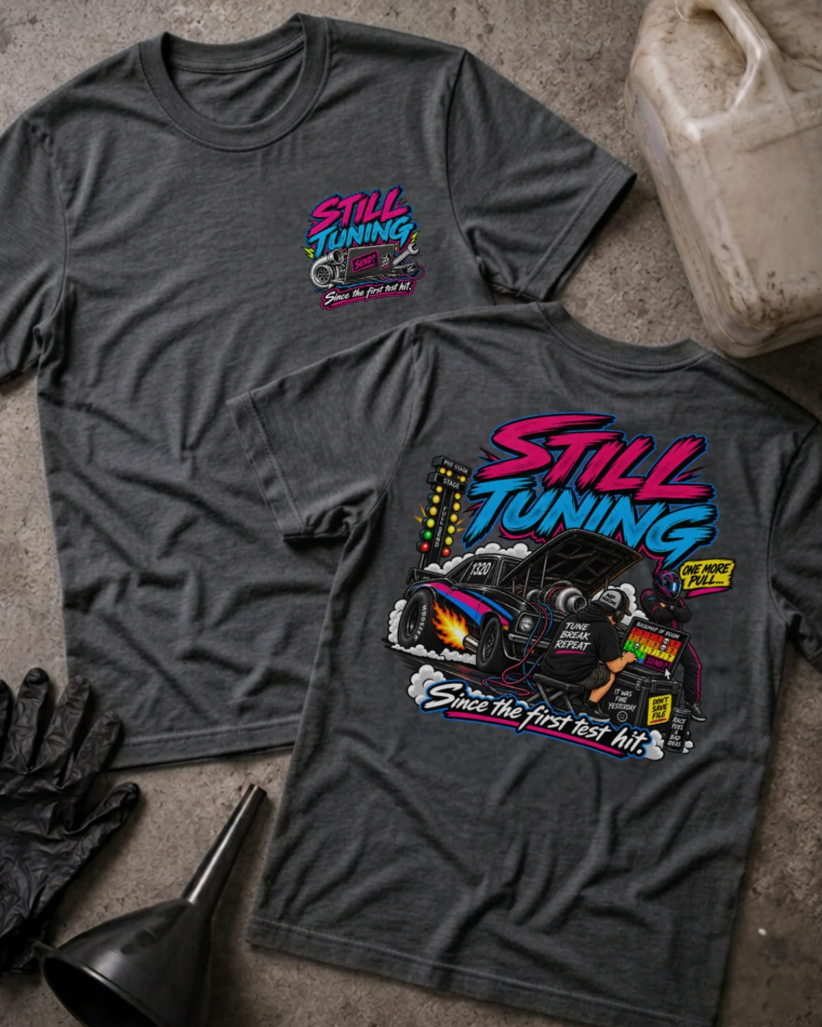 Front and back of Still Tuning navy T-shirt with chest logo, mechanic using a laptop beside a drag car with open hood, and “Since the first test hit” slogan.