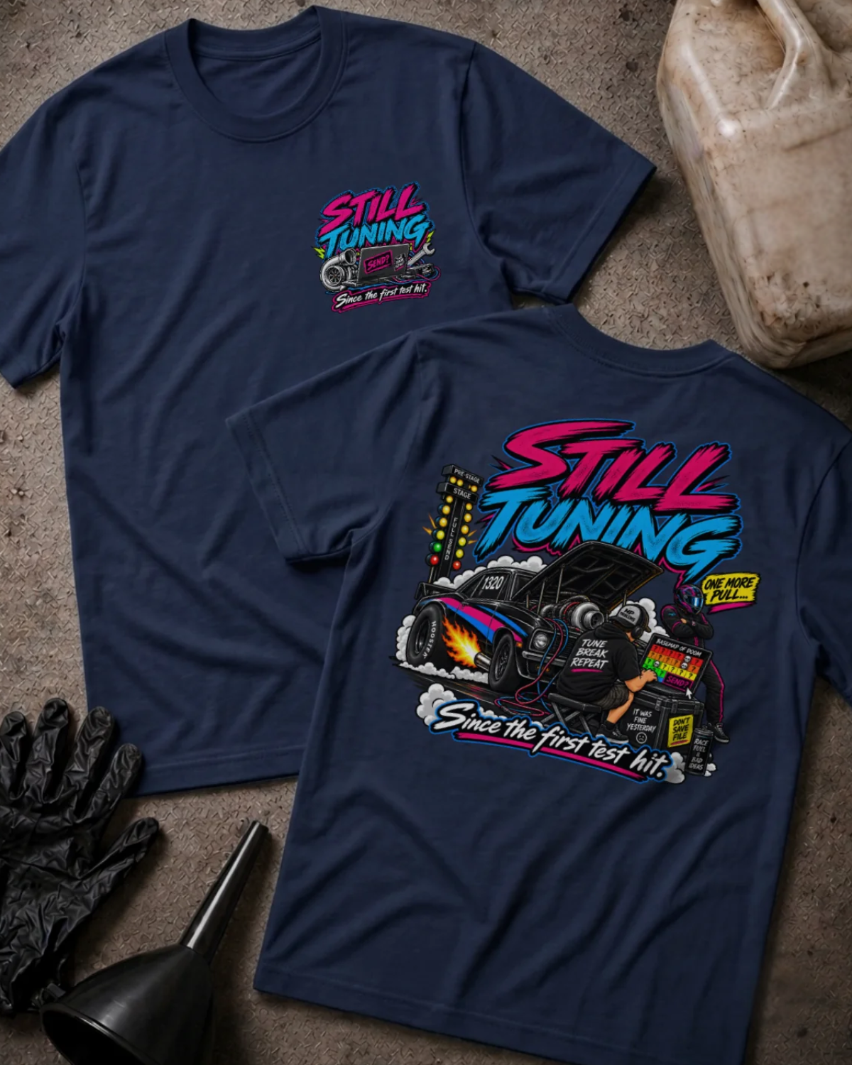 Front and back of Still Tuning navy T-shirt with chest logo, mechanic using a laptop beside a drag car with open hood, and “Since the first test hit” slogan.