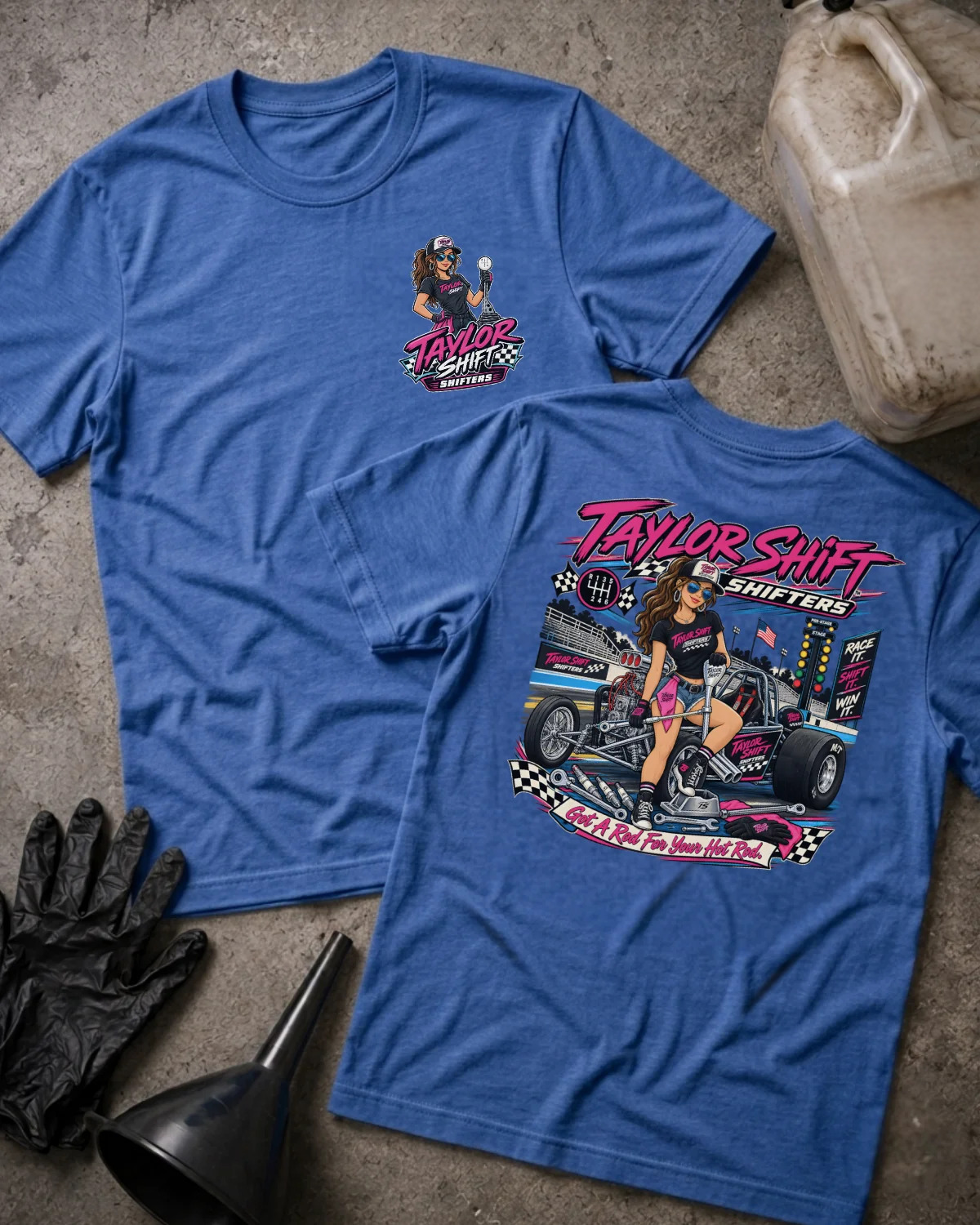 Two heather blue graphic T-shirts laid flat on a concrete surface, showing the front and back designs. The shirts feature a racing-themed illustration with the text 'Taylor Shift Shifters' and a pit crew scene.