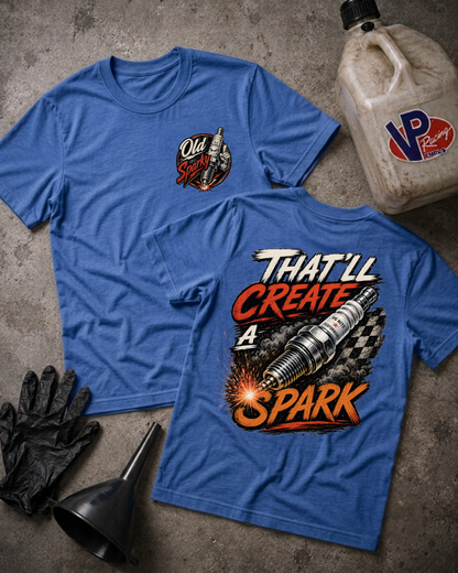 Two blue graphic T-shirts laid flat on a textured gray surface, with a black funnel, black gloves, and a VP Racing jug nearby. The front shirt has a small chest logo reading Old Sparky, and the back shirt has a large graphic with the text 'THAT'LL CREATE A SPARK' and a spark plug over a checkered pattern.