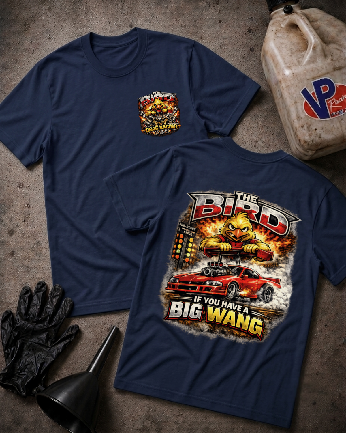 Two navy blue graphic T-shirts laid flat on a textured gray surface, with a black oil bottle, black gloves, and a black funnel around them. The front shirt shows a small multicolor chest graphic, and the back shirt shows a large graphic with the words 'THE BIRD' and 'IF YOU HAVE A BIG WANG' above and below a red sports car and a yellow bird illustration.