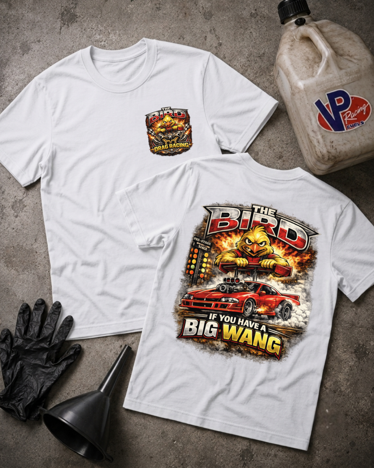 Two white graphic T-shirts laid flat on a gray concrete-style surface, with a black funnel, black gloves, and a plastic jug nearby. The front shirt shows a small chest graphic, and the back shirt shows a large colorful graphic with the text 'The Bird' and 'If You Have A Big Wang.