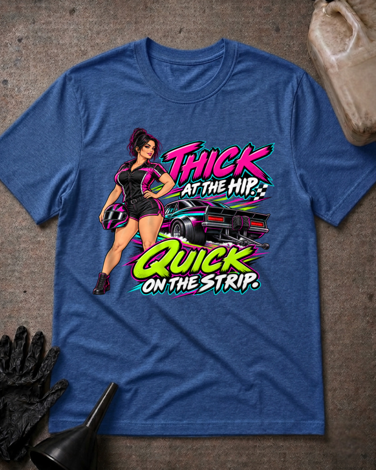 Heather true royal blue T-shirt laid flat with a woman holding a racing helmet beside a drag car and neon lettering reading “Thick at the Hip. Quick on the Strip.”