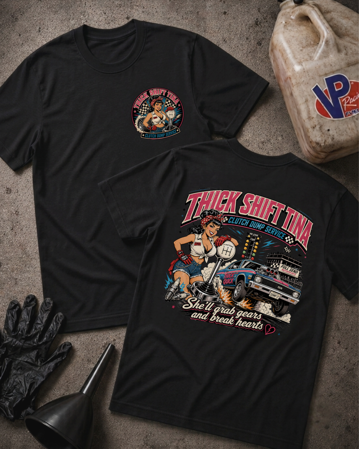 Two black graphic T-shirts laid flat on a textured gray surface, showing the front and back designs. The front shirt has a small circular chest graphic, and the back shirt has a large colorful graphic with the text 'THICK SHIFT TINA' and 'She'll grab gears and break hearts.