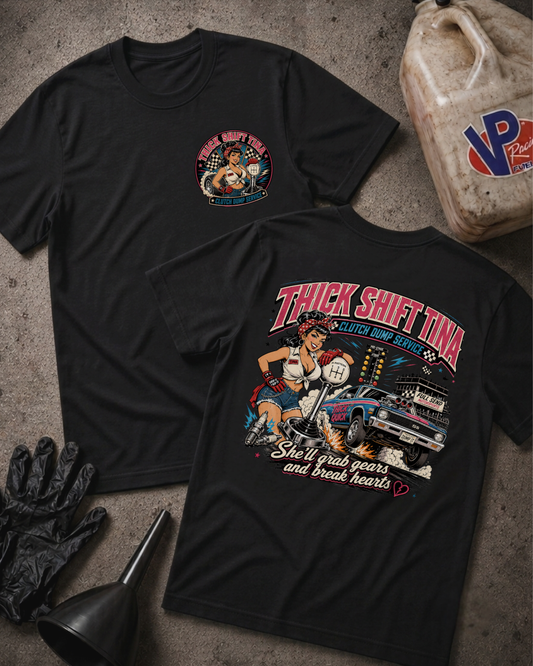 Two black graphic T-shirts laid flat on a textured gray surface, showing the front and back designs. The front shirt has a small circular chest graphic, and the back shirt has a large colorful graphic with the text 'THICK SHIFT TINA' and 'She'll grab gears and break hearts.