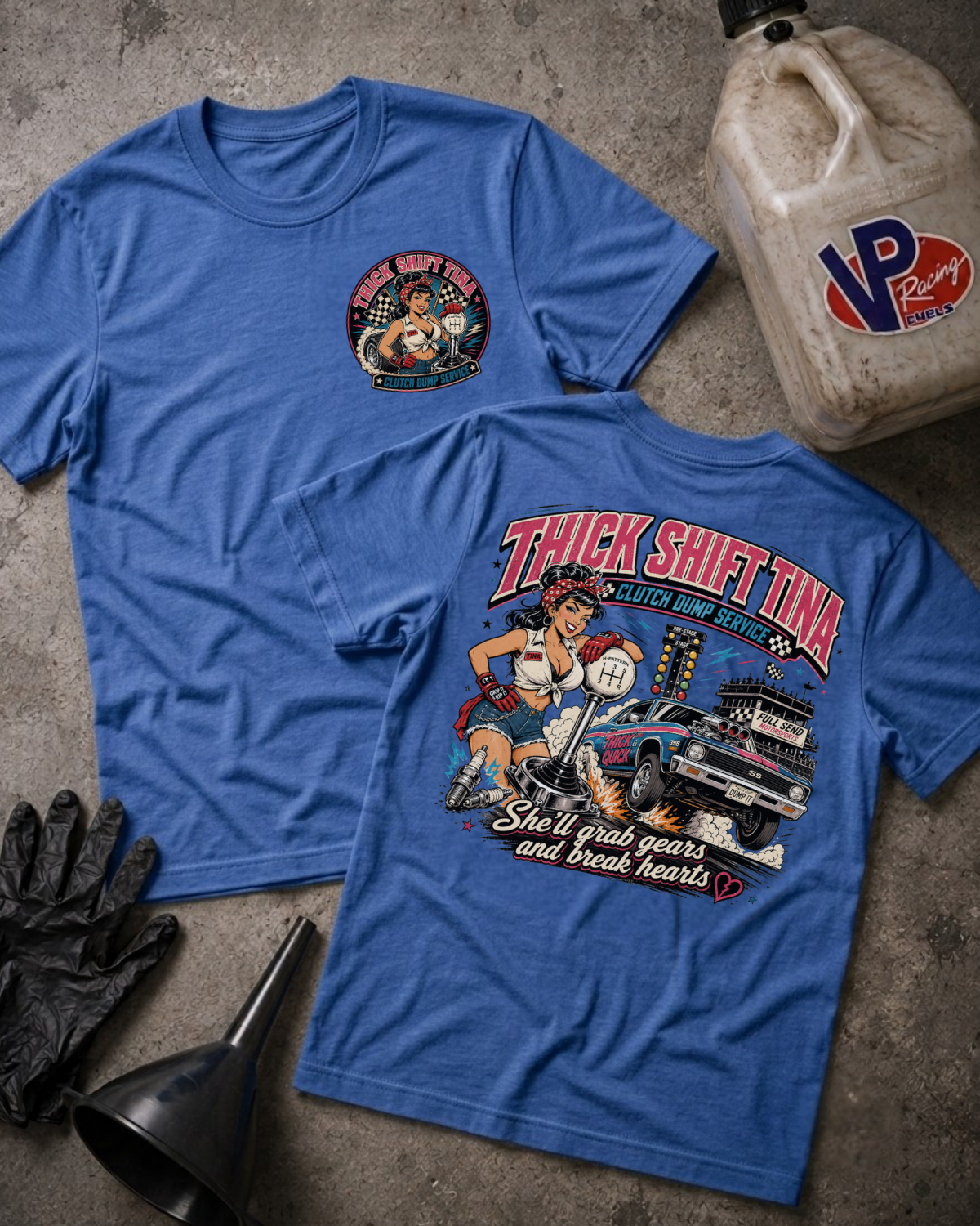 Two blue graphic T-shirts laid flat on a textured gray surface, with a vintage oil change jugs, black gloves, and a funnel around them. The front shirt shows a small circular chest graphic, and the back shirt shows a large retro-style racer graphic with the text 'THICK SHIFT TINA' and 'She'llgrab gears and break hearts.