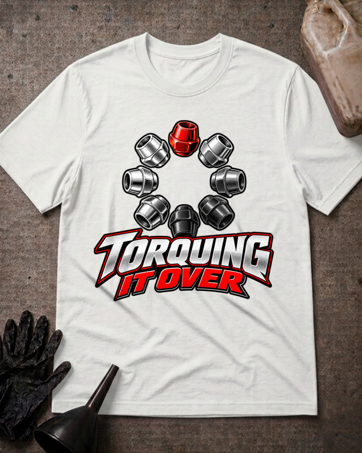 White T-shirt laid flat with a ring of silver and black lug nuts, one red lug nut at the top, and bold silver and red “Torquing It Over” lettering.