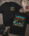 Two black graphic T-shirts displayed on a textured concrete surface, with a black funnel, black gloves, and a worn plastic jerrycan nearby. The front shirt shows a small multicolor chest graphic reading 'Track Preppers' with a monster truck illustration.