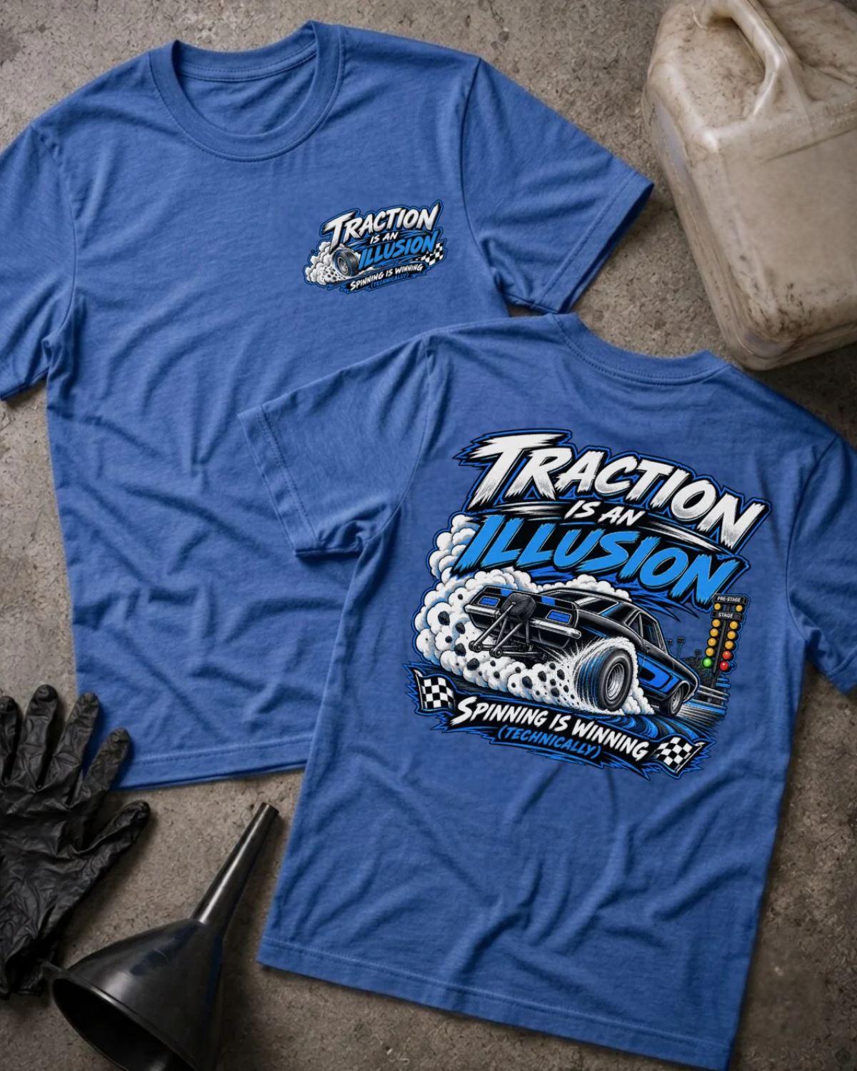 Front and back of Traction Is an Illusion heather true royal T-shirt with chest logo, black and blue drag car doing a burnout beside staging lights, and “Spinning is winning (technically)” slogan.