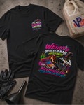 Two black graphic t-shirts displayed on a textured concrete surface with garage-themed props including a plastic jug, black gloves, and a funnel. The front shirt shows a small pink and blue logo on the left chest, while the back shirt features a large colorful graphic of a woman in a pink car with the text 'Wendy's Wheelie Bar Adjustment Keeping It Up'.