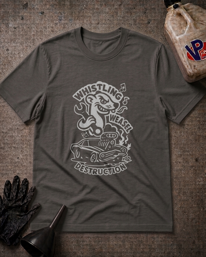 A dark gray crewneck t-shirt with a white graphic print of a cartoon weasel driving a car and the words 'Whistling Weasel Destruction'. The shirt is laid flat on a textured gray surface with automotive-themed props including a black glove, funnel, and a plastic jug.