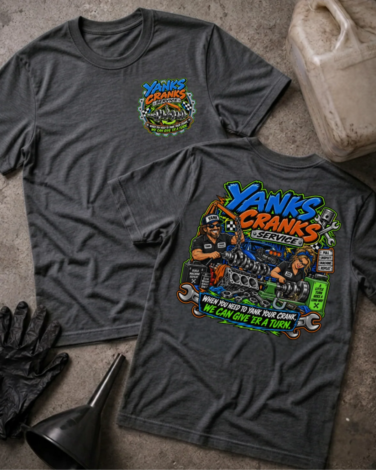 Front and back of Yank’s Cranks Service dark grey heather T-shirt with chest logo, two mechanics working on crankshafts, and “When you need to yank your crank, we can give ’er a turn” slogan.