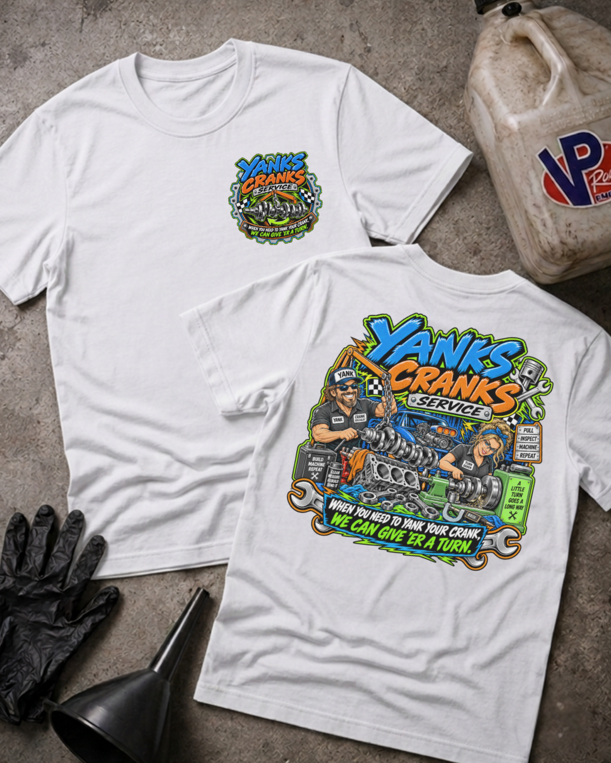 Two white graphic T-shirts laid flat on a concrete surface, showing the front and back designs. The front has a small multicolor chest graphic, and the back has a large colorful engine illustration with the text 'Yanks Canks Service' and 'When You Need To Yank Your Crank We Can Give 'Er A Turn'.